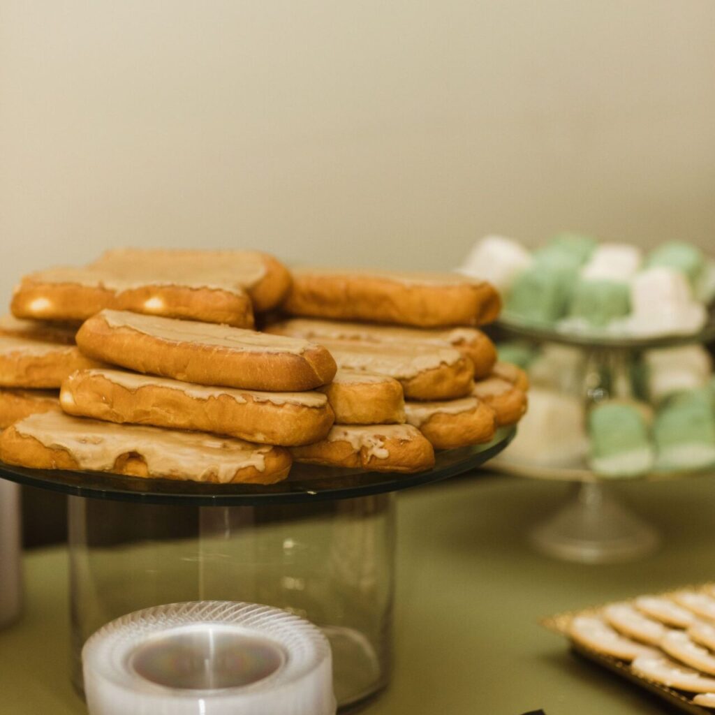 Maple donuts with glossy maple glaze arranged on a tiered glass display stand, ready to serve at a bakery or event.